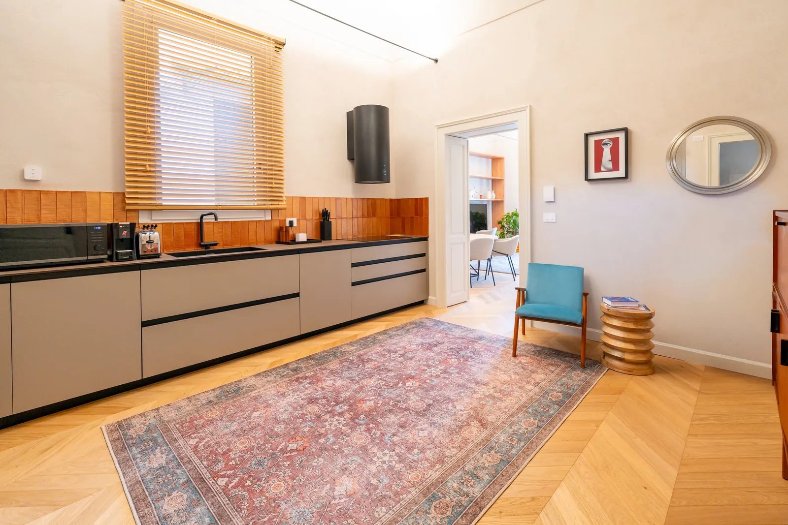 Cucina con mobili grigi e piastrelle color terracotta, tappeto persiano e poltrona azzurra