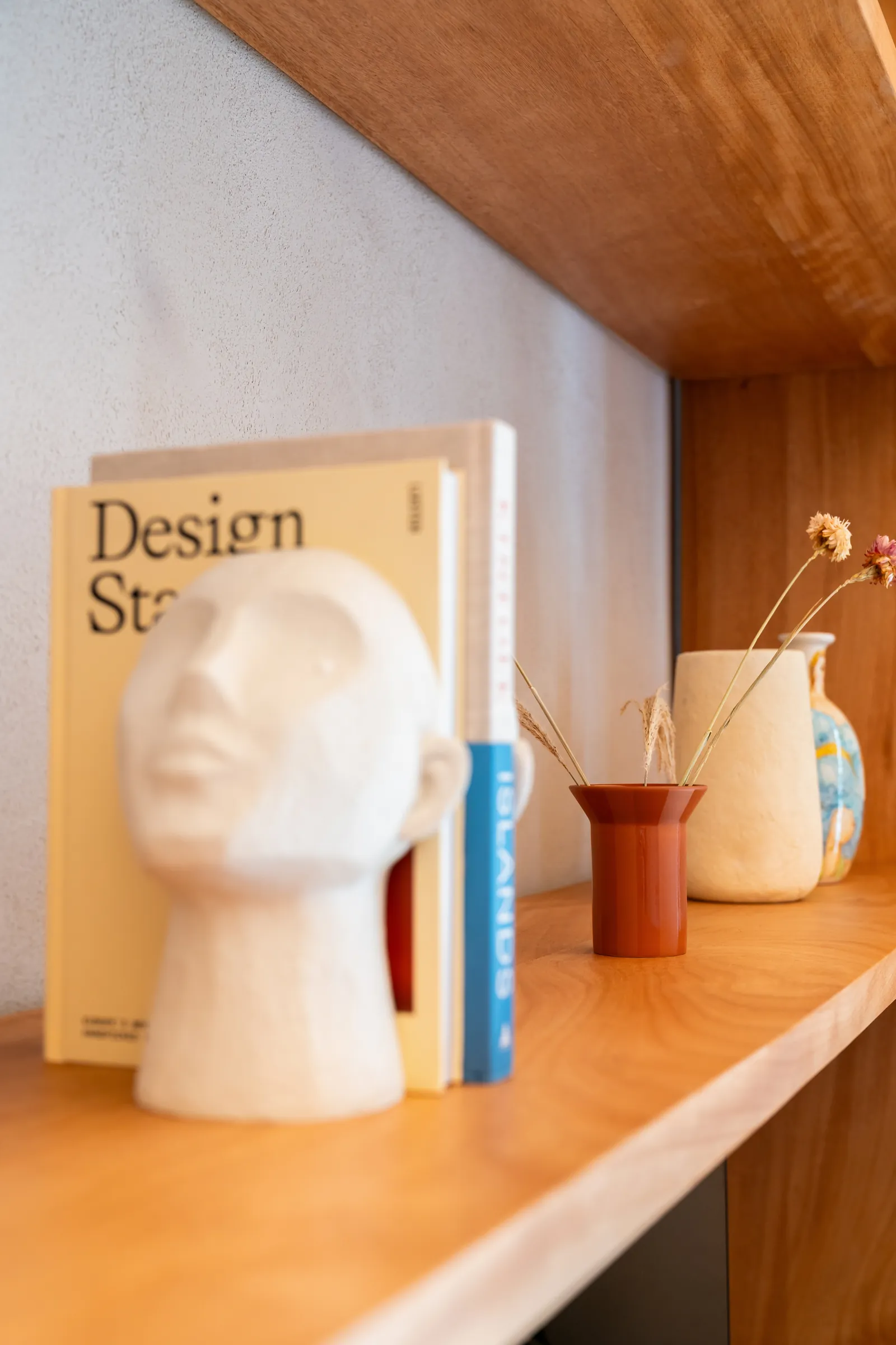 Mensola con libri di design, testa in ceramica bianca e vaso rosso